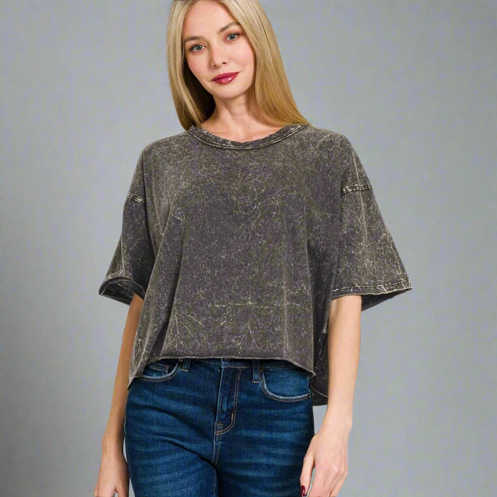 Woman wearing an ash black distressed t-shirt and blue jeans on a white background