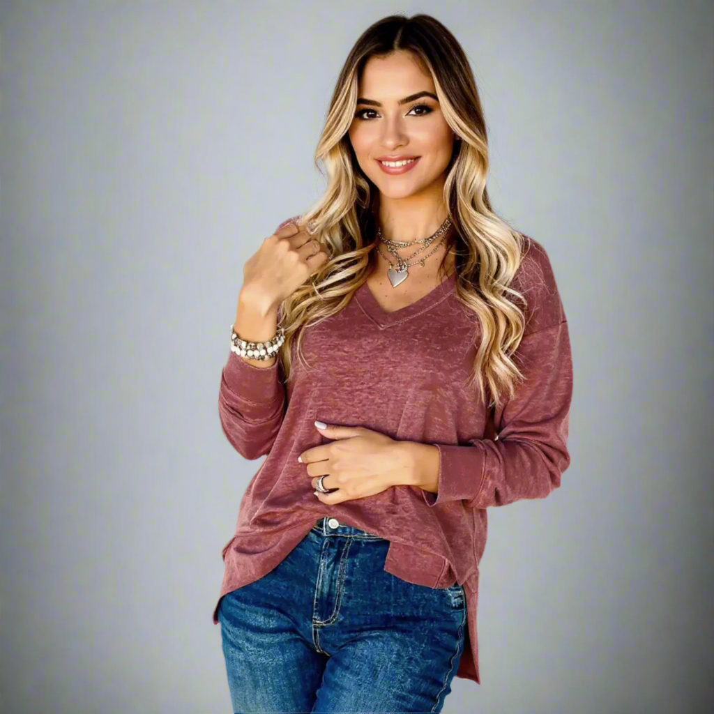 Woman wearing a maroon long-sleeve top and blue jeans on a gray background