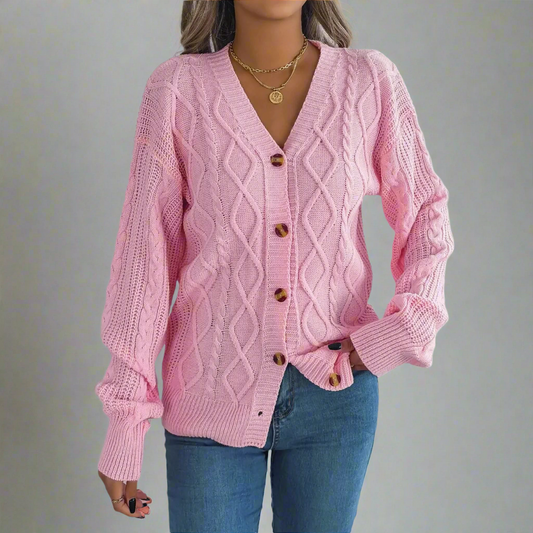 Person wearing a pink cable knit cardigan with brown buttons on a neutral background