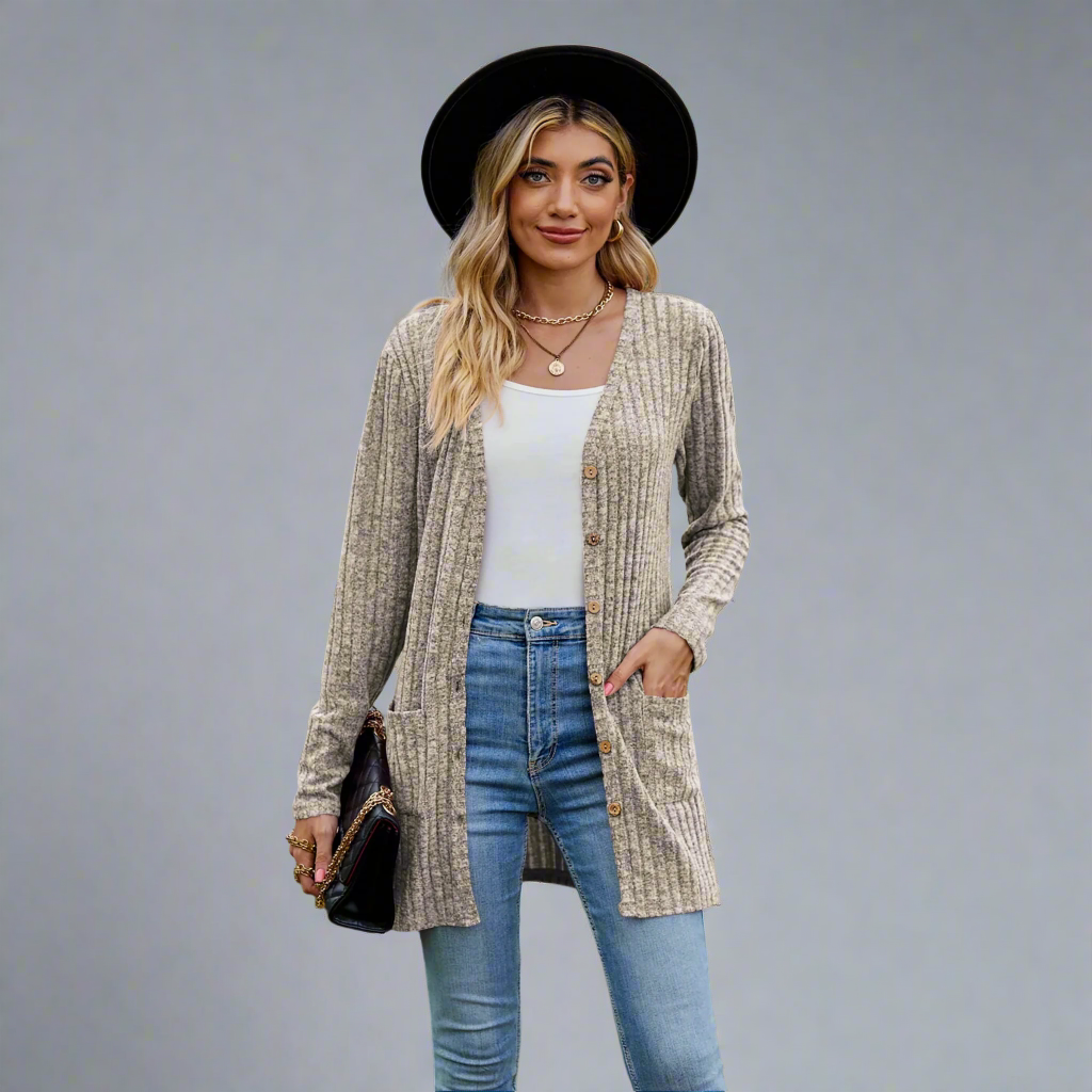 Woman wearing a beige cardigan, white top, blue jeans, and black hat outdoors.
