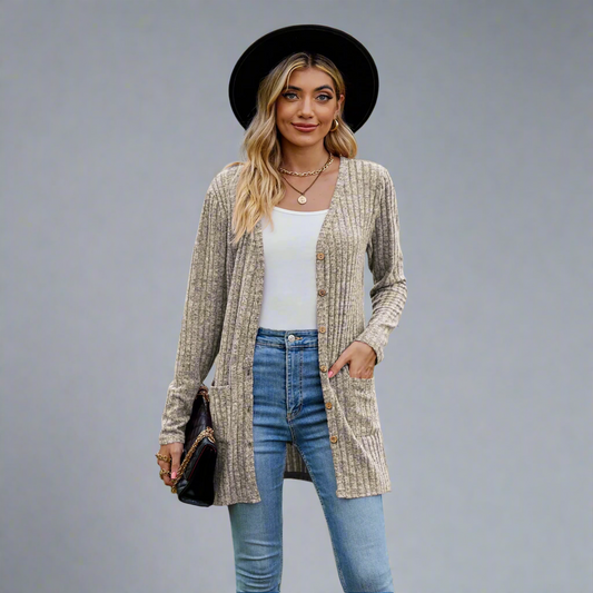 Woman wearing a beige cardigan, white top, blue jeans, and black hat outdoors.