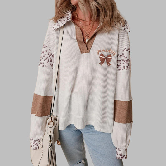 Woman wearing a white sweater with brown accents and leopard print details on a beige background
