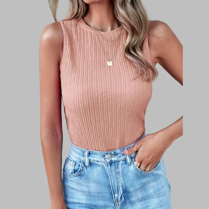 Woman wearing a pink ribbed tank top and blue jeans against a light gray wall.