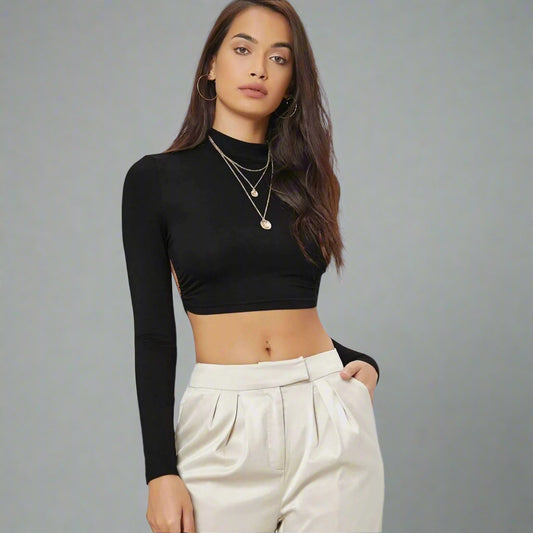 Woman wearing a black long-sleeve crop top and white pants against a neutral background