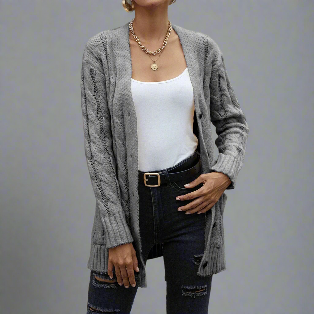 Person wearing a gray cable knit cardigan over a white top and black pants in a forest setting.