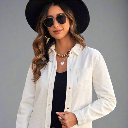 Woman wearing a white denim jacket, black hat, and sunglasses on a gray background