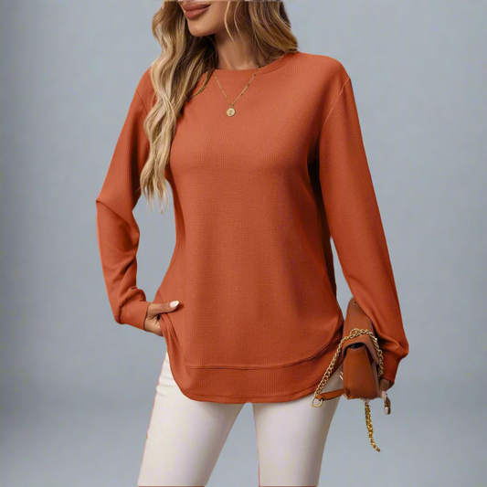 Person wearing a rust-colored long-sleeve top with a plain background
