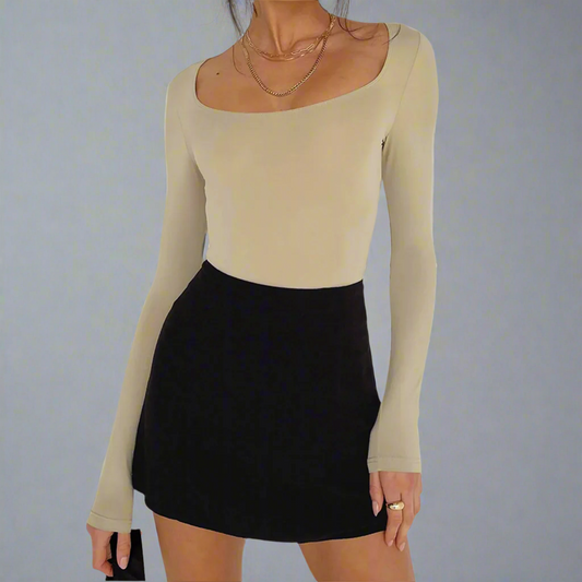 Person wearing a beige long-sleeve top and black skirt against a plain background